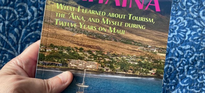 A hand holding a book with the cover text "Remembering Lahaina: What I Learned about Tourism, the ‘Āina, and Myself during Twelve Years on Maui."